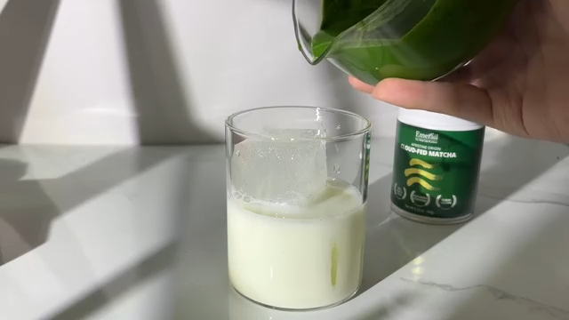 Hand pouring matcha from Emerail tin into a glass of pale green whisked drink