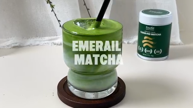 Glass of whisked green matcha on a stand with a small Emerail cloud-fed tin